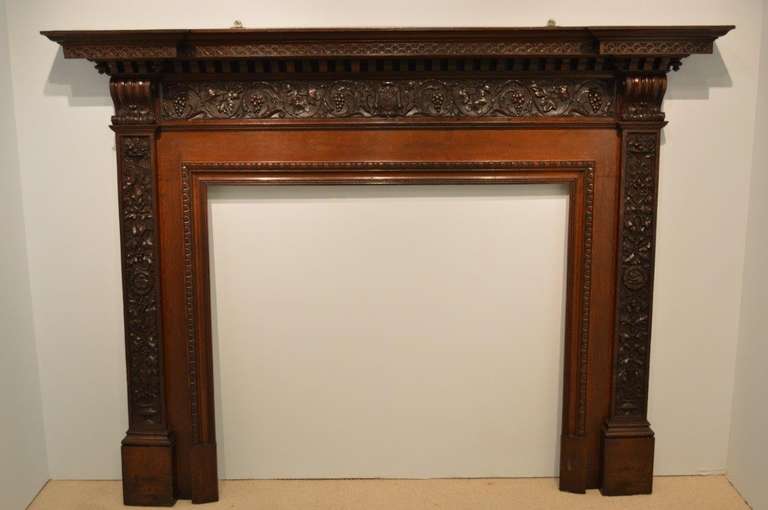 A carved oak Victorian Period antique fire surround. Having an inverted breakfront mantle with traditional carved detail above the beautifully carved vine, grape and oak leaf frieze, with a central carved armoreal depicting thistles. The jambs with
