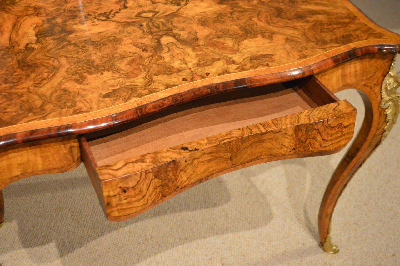 A Burr Walnut, amboyna & Ormolu 19th Century French style Library Table. The top of serpentine outline veneered in beautifully figured burr walnut with amboyna banding and a goncalo alves moulded edge. The frieze veneered in finely figured walnut