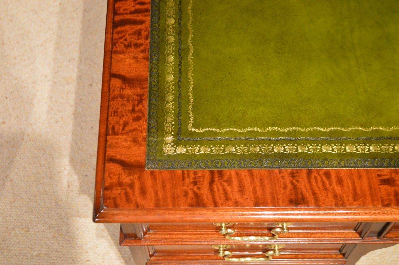A Stunning quality mahogany Late Victorian/Edwardian Period antique desk by Gillows. Having a rectangular top veneered in the finest figured mahogany and with an inset olive green blind and gilt tooled leather writing surface above an arrangement of