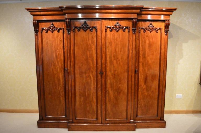 A very good mahogany Early Victorian Period four door breakfront antique wardrobe. The breakfront moulded cornice above an arrangement of four beautifully figured mahogany doors, each with bold applied carved detail and raised flat pilasters with