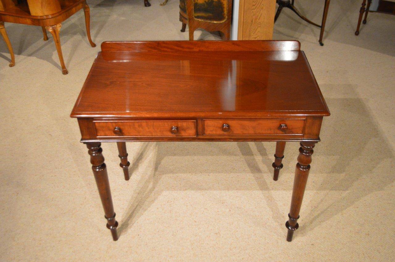 A mahogany Early Victorian Period two drawer antique side table. The rectangular solid mahogany top having a small raised rear gallery above two rectangular mahogany lined frieze drawers, each having the original mahogany turned drawer pulls.