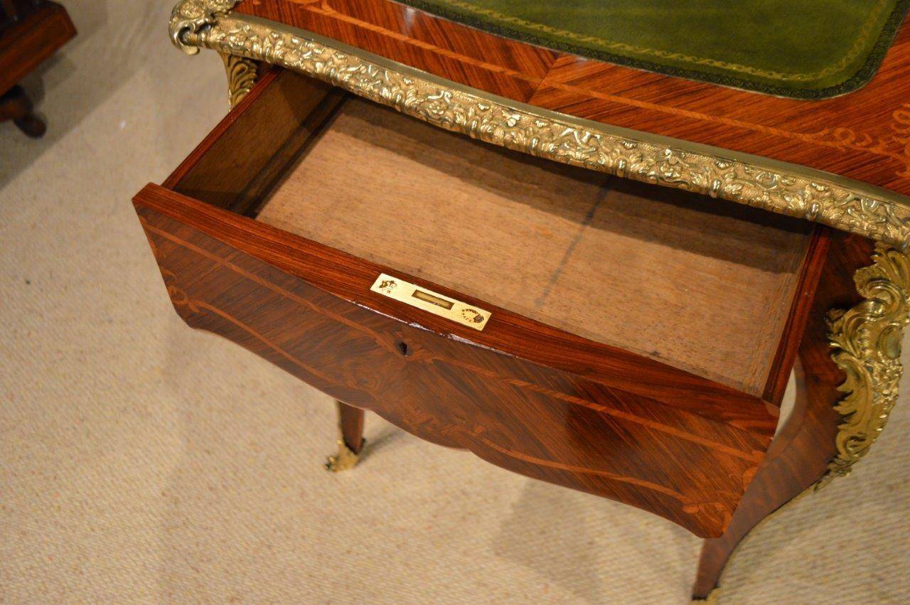 A beautiful kingwood and ormolu mounted Victorian period antique writing table. The top is veneered in kingwood with tulipwood cross banding and an olive green tooled inset leather writing surface with a cast ormolu beaded edge. Having a gentle