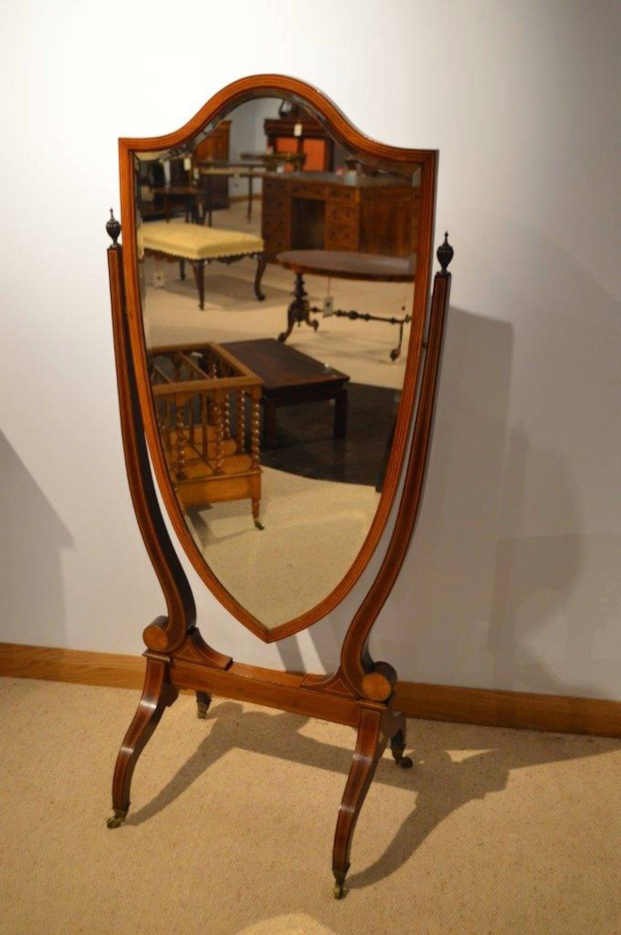 A beautiful mahogany inlaid Edwardian period antique cheval or dressing mirror. Having a shield shaped bevelled mirror with simple boxwood line inlaid detail, supported on lyre ends with beautifully carved mahogany finials and shell inlaid paterae.