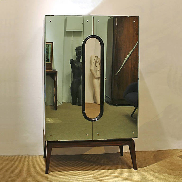 Art Deco dry bar, french polished mahogany veneer, doors with pale green mirrors, central oval medallion mirror, black lacquered wood frame, compartmentalized maple interior, chrome plated brass hardware.
Italy circa 1930