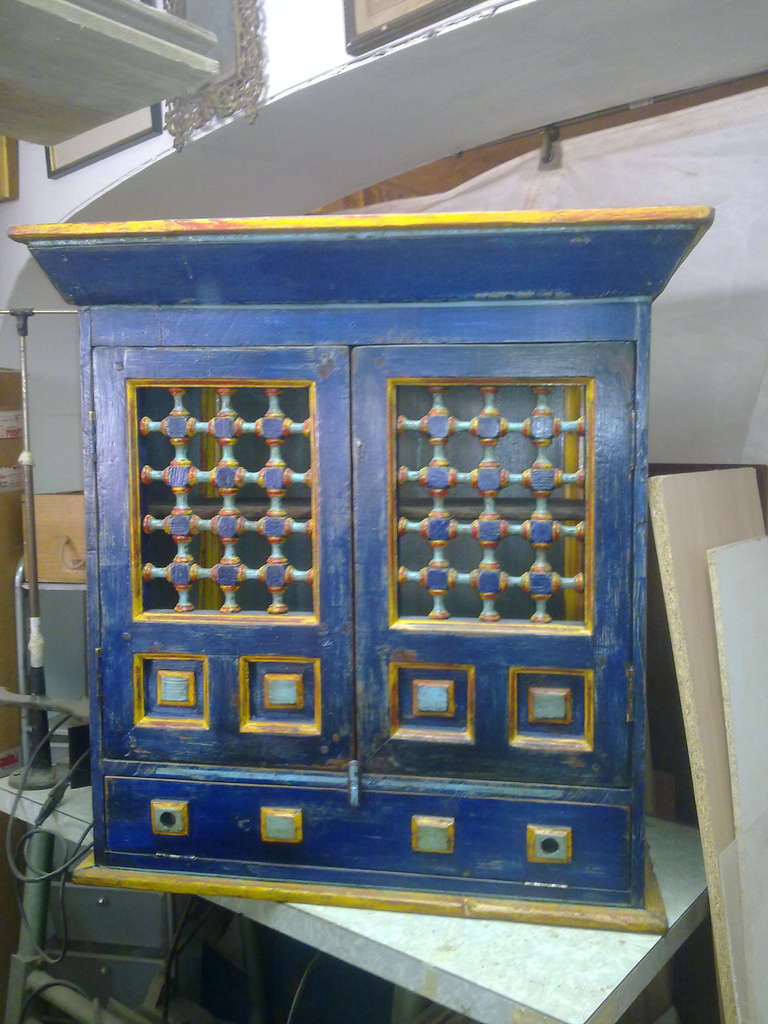 A wall hanging or surface sanding cabinet, with bobbing doors, polychromed in electric blue, with gold and pale blue detail. Signed MSimpson.