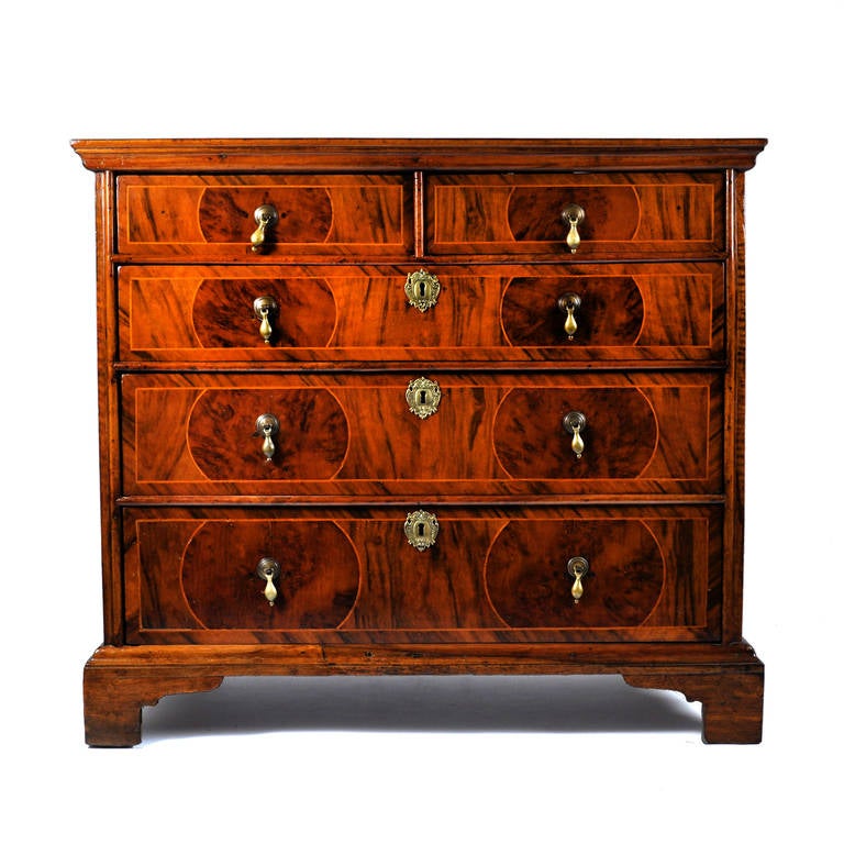 For sale on 1st dibs a Queen Anne commode on walnut and yew wood. This English piece from the 18th century has two-sided drawers and three long drawers on bracket feet. The geometrical and simetrical veneered top is made with perfection. The honey