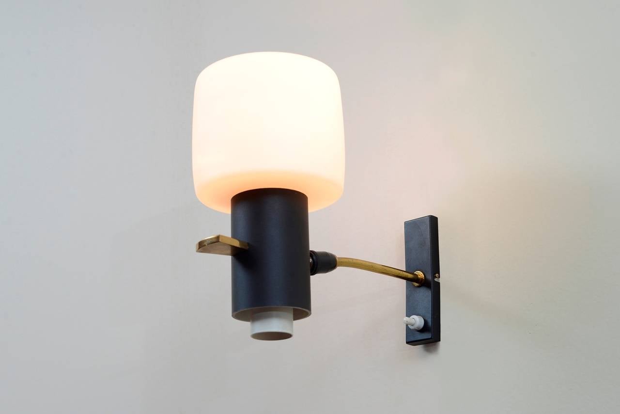 A pair of wall sconces in brass, frosted glass and black painted metal.