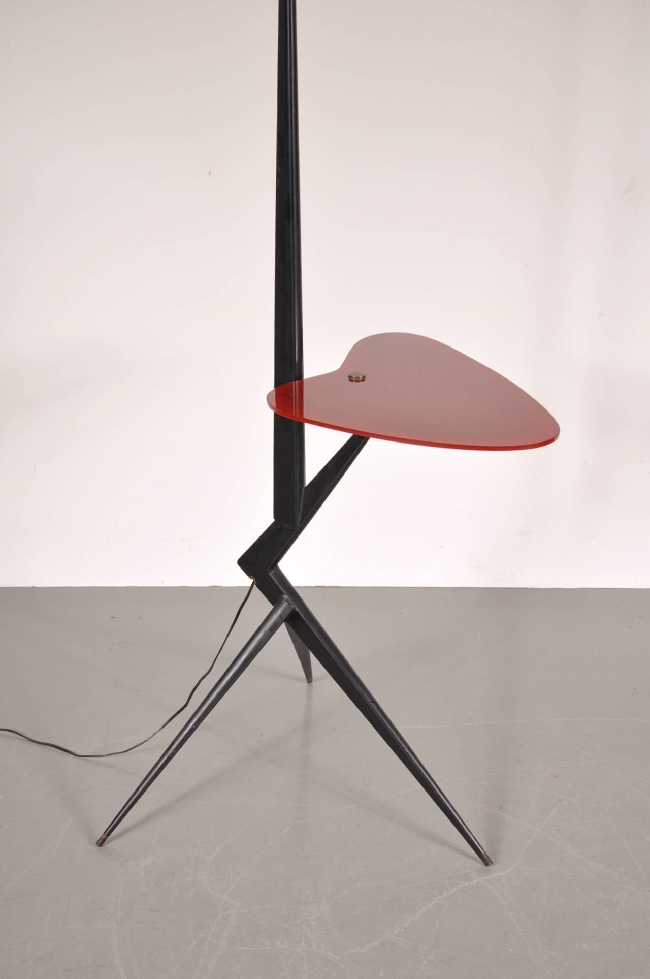 Very rare floor lamp attributed to Angelo Ostuni, manufactured around 1950.

The lamp has a black metal base with three legs and a unique folded part leading to a small red glass side table top. It has a white fabric hood. All together this lamp