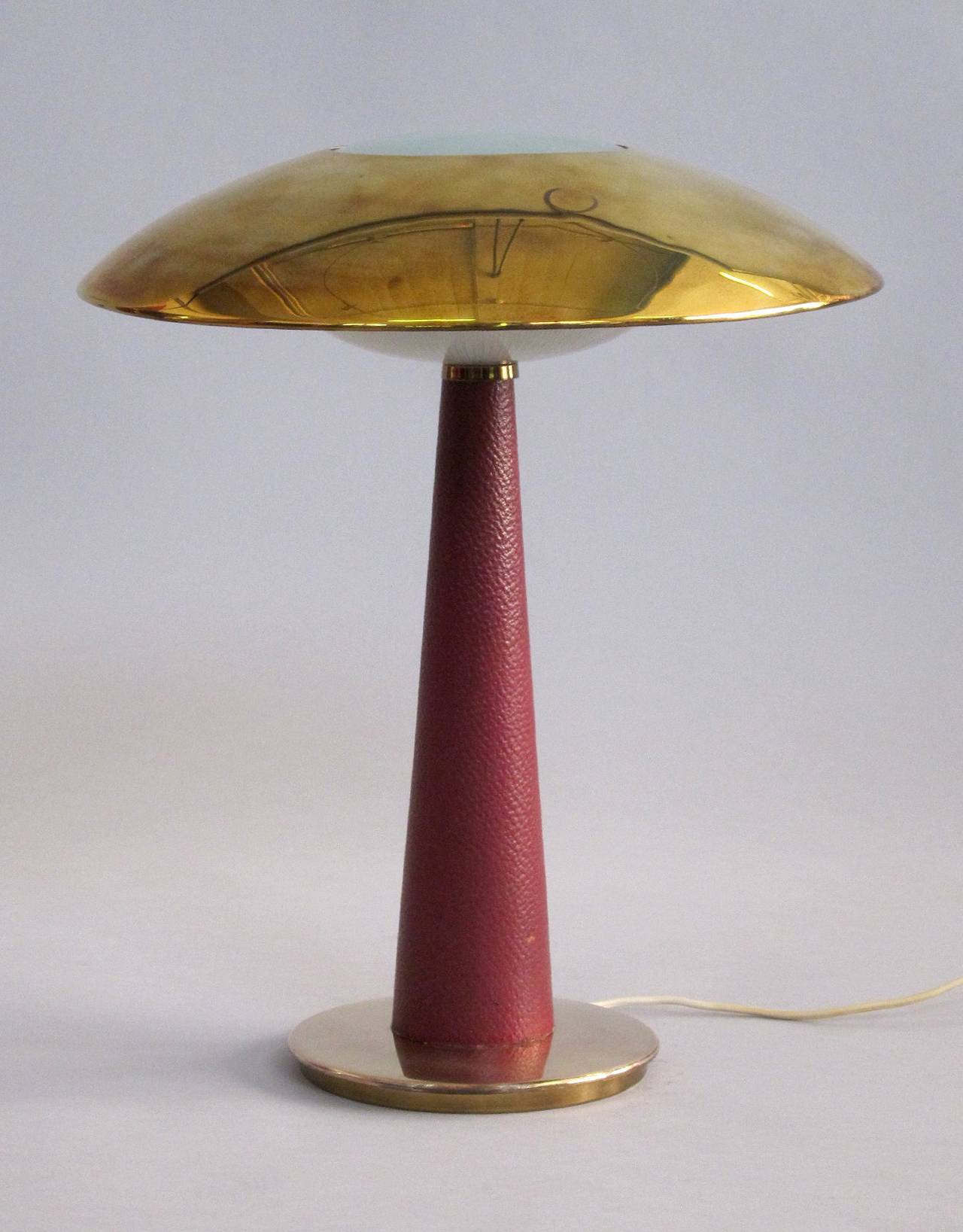 The opening in the brass shade is covered by a convex, sanded glass.
Under the brass shade there is a corrugated cast glass, which covers the two fixtures. The stand is covered with red leather.