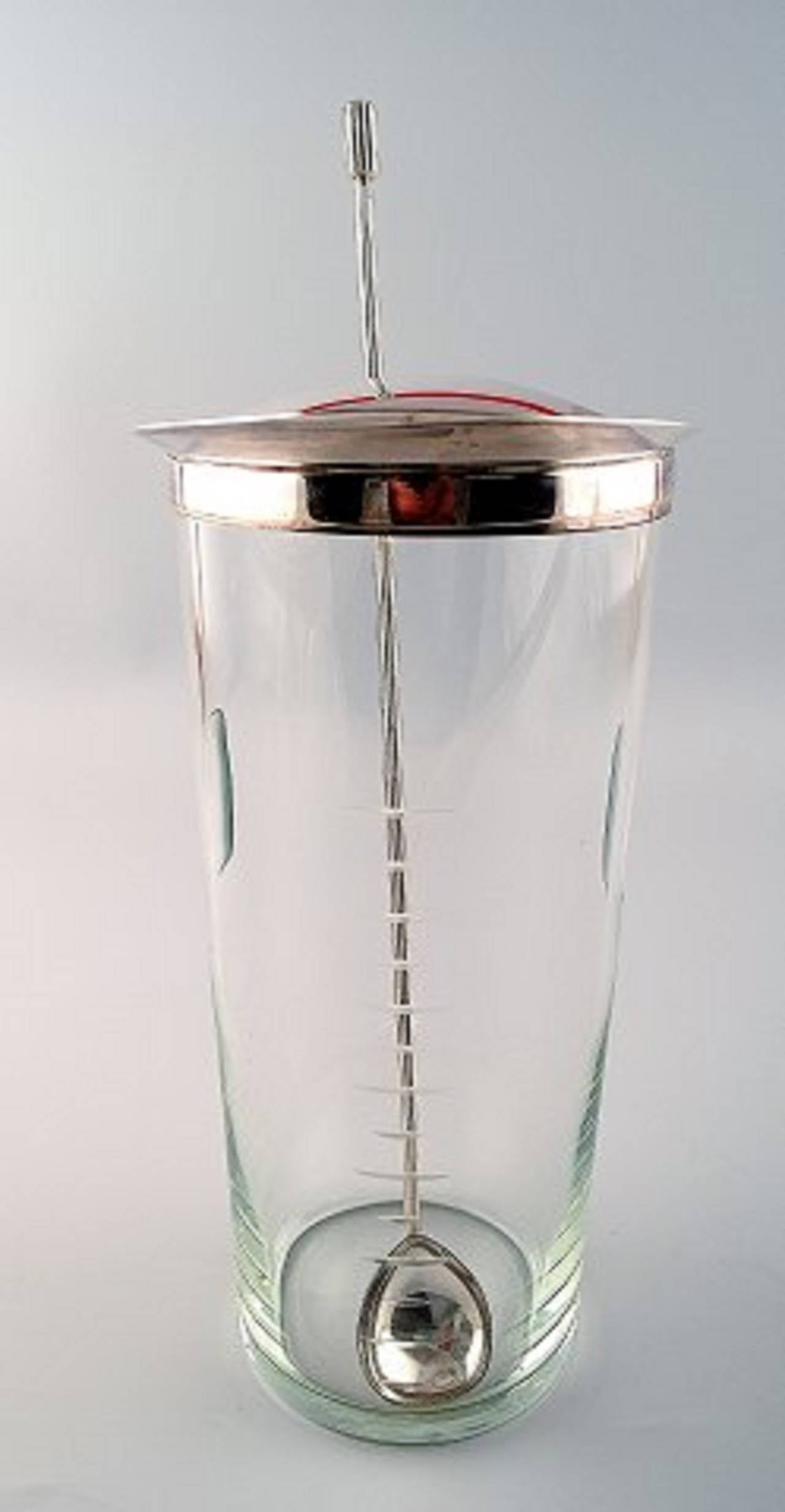 Ole Hagen, b.1913, d.1984
Clear glass cocktail pitcher with mounting and stirring spoon of sterling silver.
Made and stamped by A. Michelsen.
Spoon weight 44 gr. Measures: L 29.5cm. Pitcher H 23.5cm.
In perfect condition.