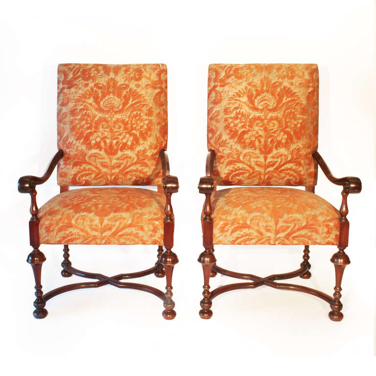 Two dark stained Armchairs made in the 20th century in William and Mary 
style.  The rectangular backs and seats are upholstered  in Claremont  Fortuny gold cotton damask.  The chairs have outscrolled arms on turned tapered legs joined with cross