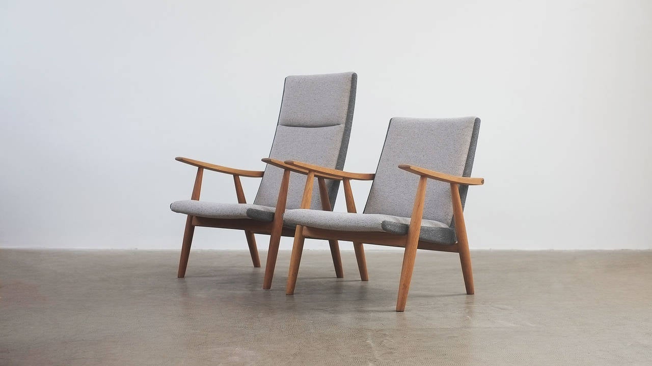 Fantastic pair of Hans Wegner GE260 armchairs. Solid oak frames with brass details. Fully reconditioned and reupholstered in two-tone grey fabric. Amazing pair of chairs.