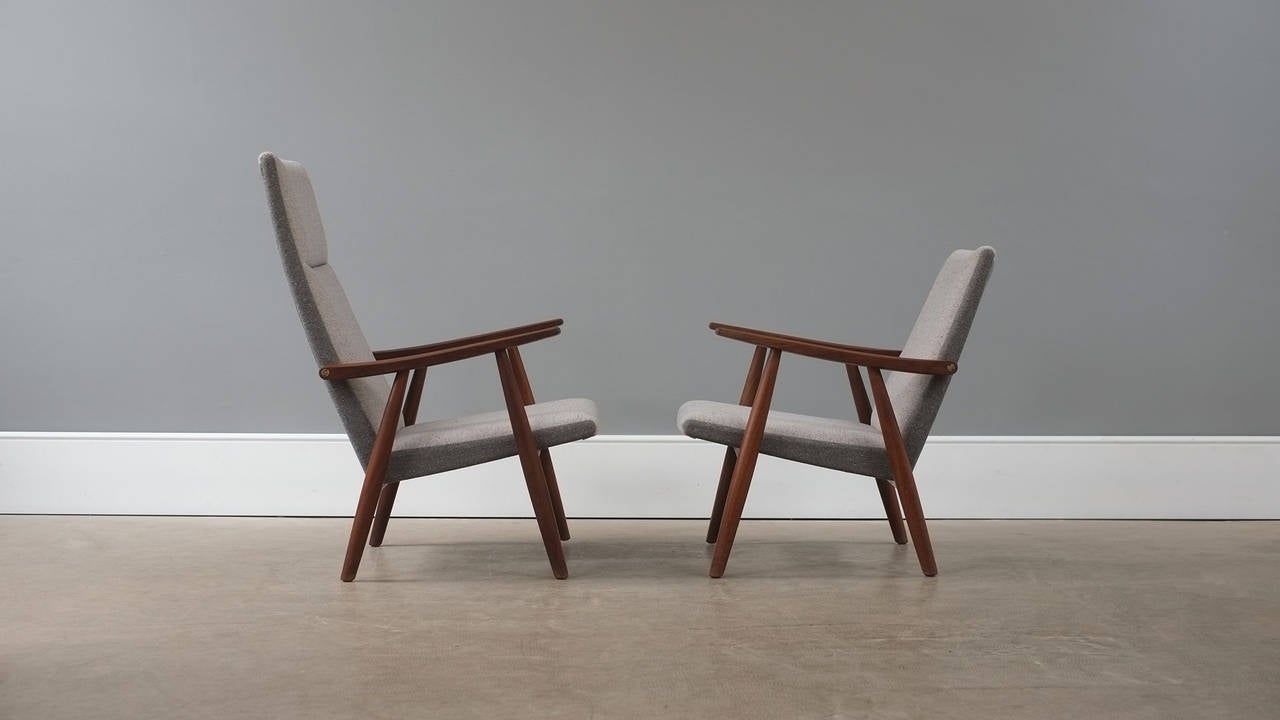 Fantastic pair of Hans Wegner GE260 armchairs. Solid teak frames with brass details. Fully reconditioned and reupholstered in two-tone grey fabric. Amazing pair of chairs.