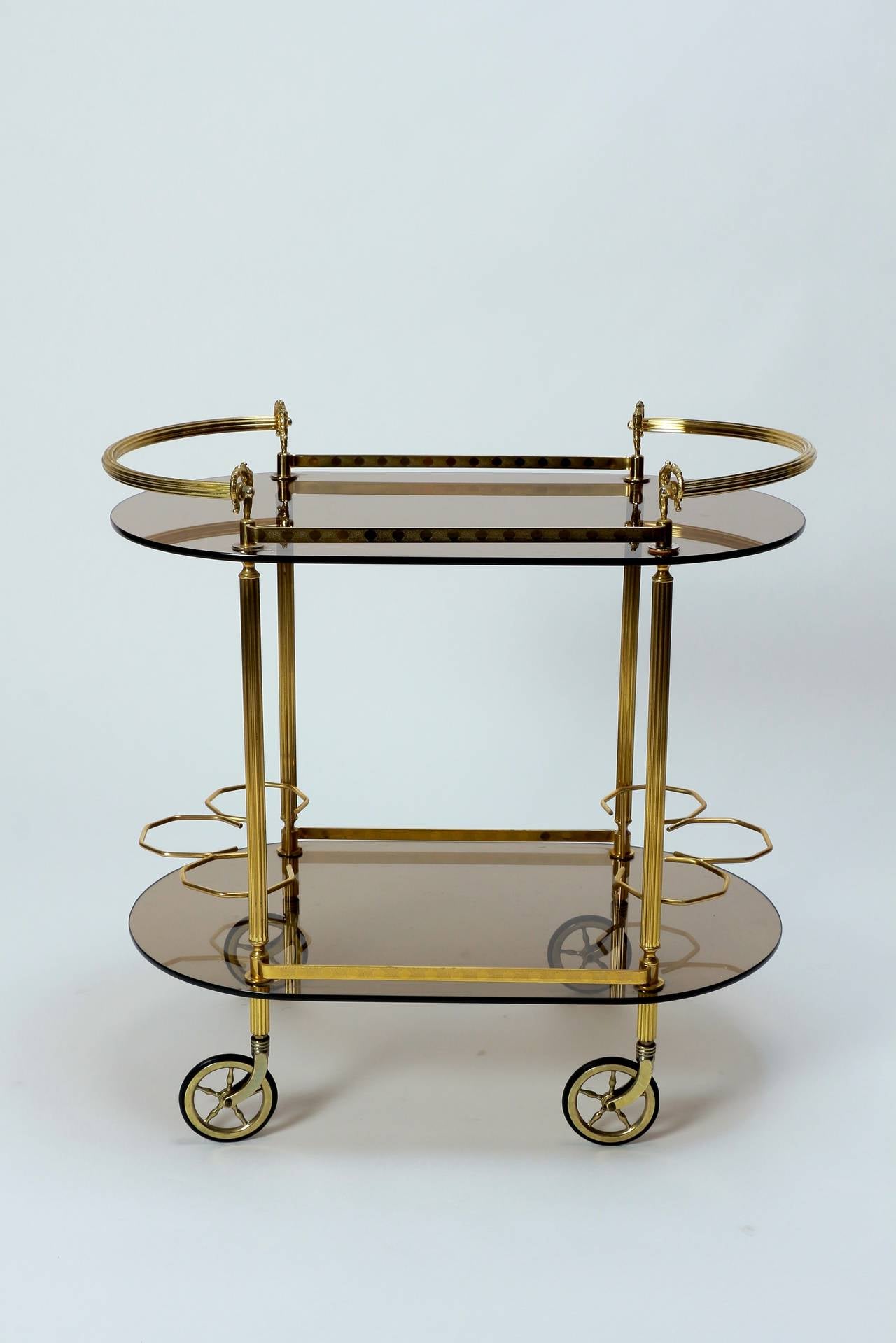 Elegant bar cart, made in France in the 1970's. High quality craftsmanship, solid brass and thick smoked crystal glass shelves. 6 bottle holders on the bottom shelf, the castors roll perfectly smooth! Great condition!