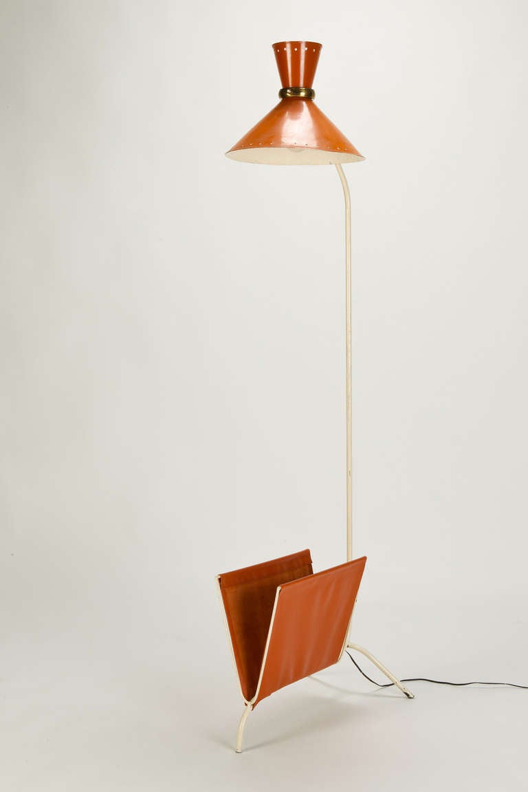 Rare floor lamp with a magazine rack in orange leather by René Mathieu for Lunel, France, 1950's. Brass ring around the lampshade with the switch attached. Two light bulbs, one to front and one to back. Cut-out stars in metal shade