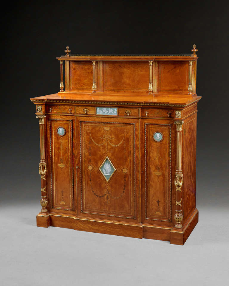 A superb satinwood breakfront cabinet by Wright and Mansfield, designed by Crosse in the Adam Revival style. The galleried superstructure supported by four reeded gilt columns with carved gilt acanthus details above three frieze drawers with a