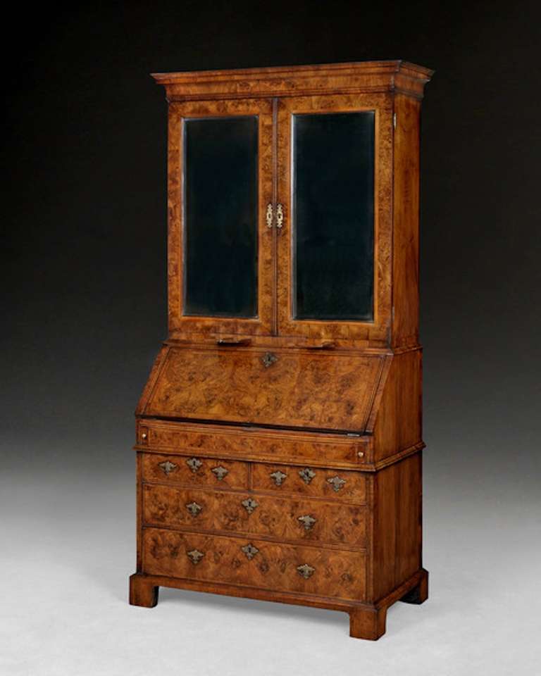 A superb Queen Anne period burr walnut bureau cabinet having a stepped, concave cornice above the two doors the top retaining the original bevelled mirror plates and fitted with adjustable shelves above a row of conforming drawers, the base with a