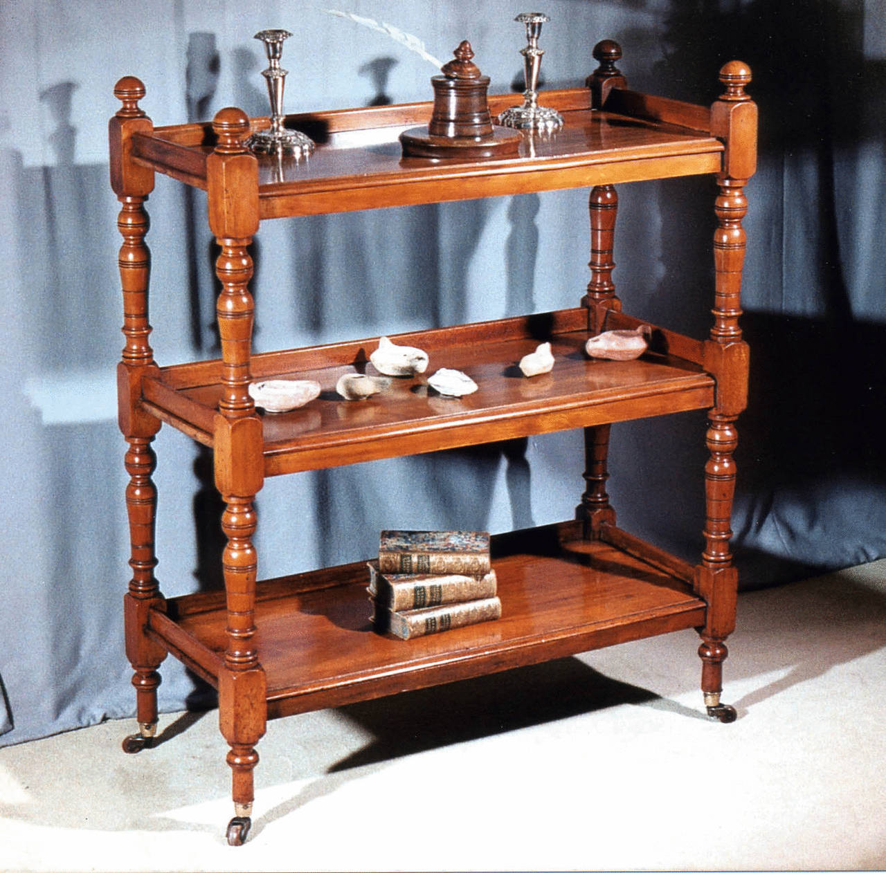 A William IV period turned walnut etagere, the three galleried shelves with turned supports and terminating in brass cups and casters.