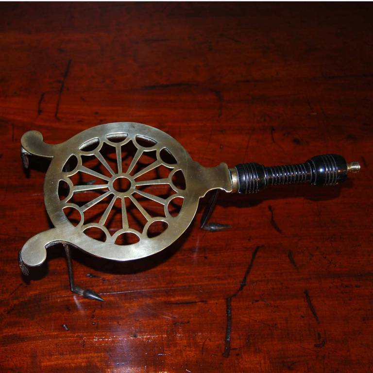 A fine and pretty George III period brass and iron trivet with a ring turned ebonized handle, the circular open fret plate with two hooks and three iron legs with pointed feet. The underside of the plate is stamped with an Orb and Cross device