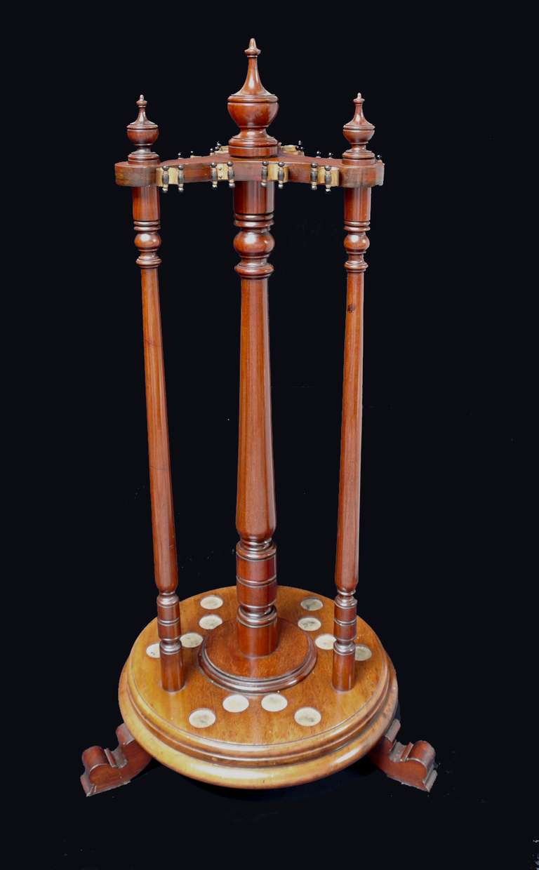 A free-standing mahogany revolving billiard cue carousel by George Wright of London circa 1880, a triform top mounted with decorative finials and original ebony brass sprung cue clips, supporting a central column flanked by three similar uprights,