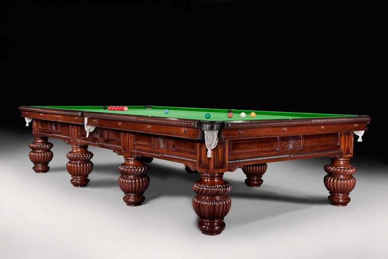A full size 12ft x 6ft mahogany billiard table standing on eight massive lobed and turned legs, the panelled side frames are embellished with gadrooned mouldings, fan shape carvings and corbel brackets. The intricate cushion friezes compliment the