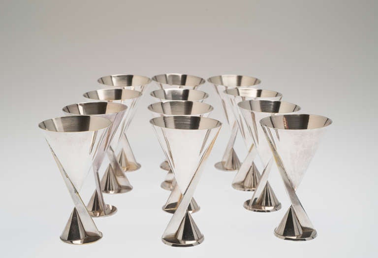 Set of 12 modernist cocktail glasses, silver plated metal; two cones pointing in opposite directions, joined by a triangular rod, on a circular base.