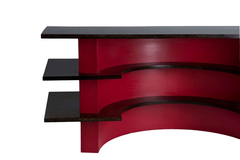 Desk made of three half-circles of wood painted in red, between which are three desktops with palm wood veneer.