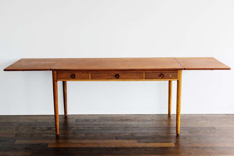 This table in teak, oak and bronze by Hans J. Wegner was made by Andreas Tuck in Denmark, circa 1955. The carved teak pulls and brass keyhole are a wonderful example of the cabinetmakers quality. It has three drawers and drop leaves on both sides,