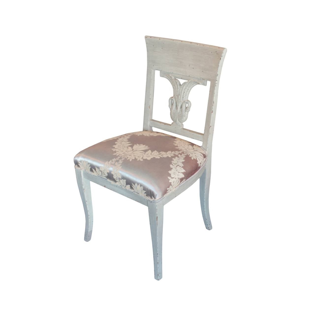 Comfortable and well proportioned, each chair having a back rest decorated with a pair of finely carved adjacent swans with elevated wings forming an urn shaped splat. Sabre legs creating four corresponding subtle klismos configurations. In painted