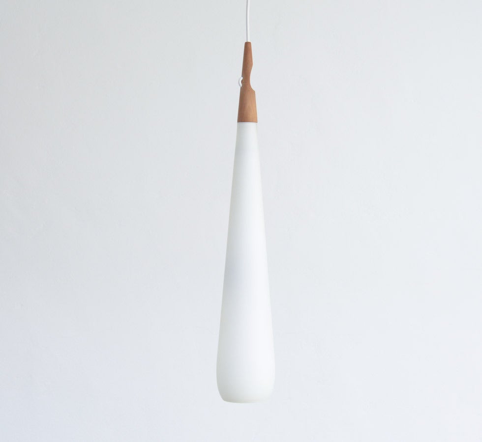 This minimal pendant lamp was designed by Uno & Östen Kristiansson for Luxus in Sweden in the 1950s.
It is a great example of Scandinavian light design.
The drop is made of opaline glass with a top in teak wood. It is very nice detailed.
This