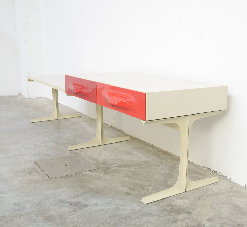 This unique low cabinet was designed by Raymond Loewy for DF2000 in 1965.
In fact it is a TV cabinet. It is a minimal cabinet with a red and an orange drawer in ABS plastic. The body is made of broken white Formica and the base of broken white