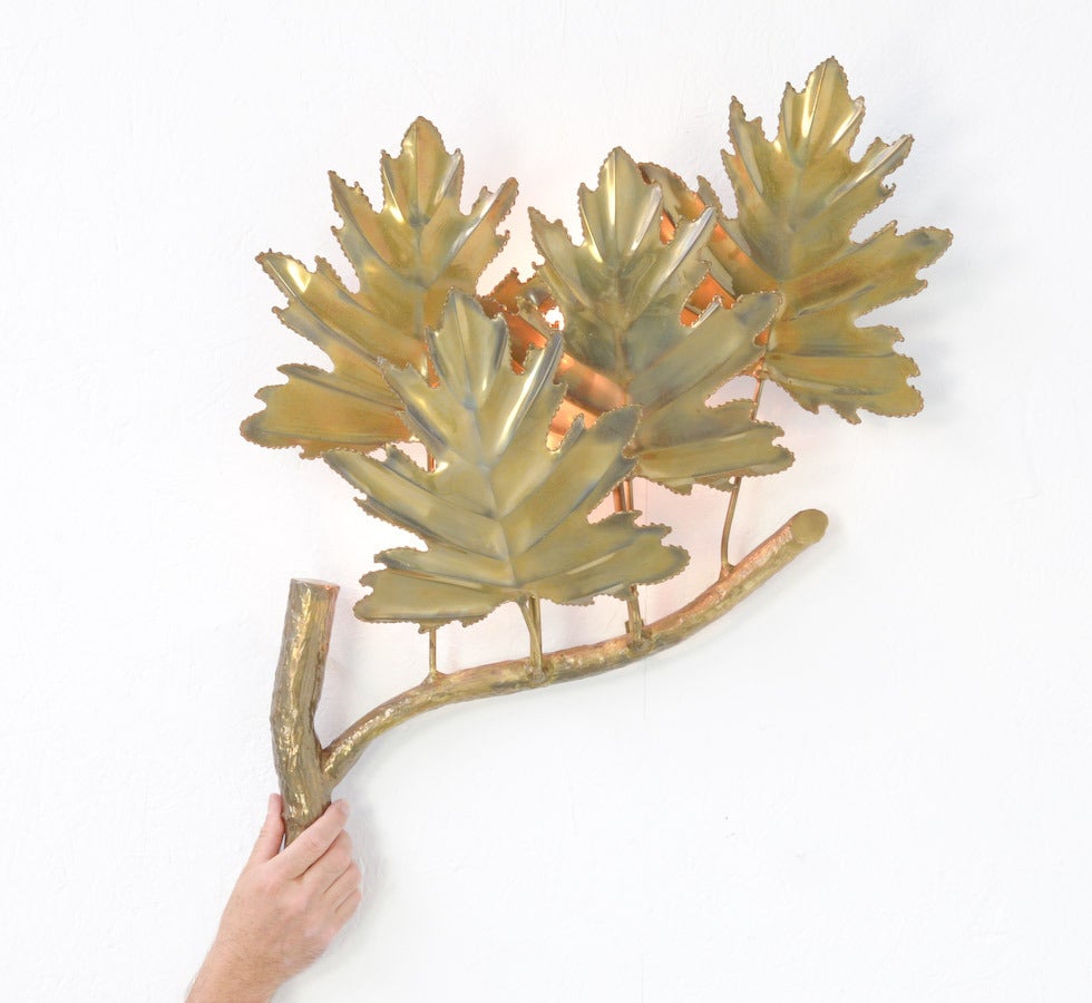 This amazing brass wall lamp is a design by the 1970s.
It is a beautiful lamp inspired by a large branch with five big leaves. It is completely made of brass and handmade. It is a unique piece of 1970s design.
On the back side are two-light bulbs.