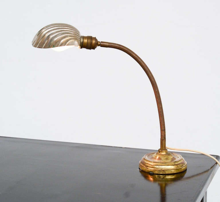 This brass desk lamp with flexible column is terminating in shell-shaped shade. It is an old piece with a porcelain socket and switch.
The lamp is in good original condition.