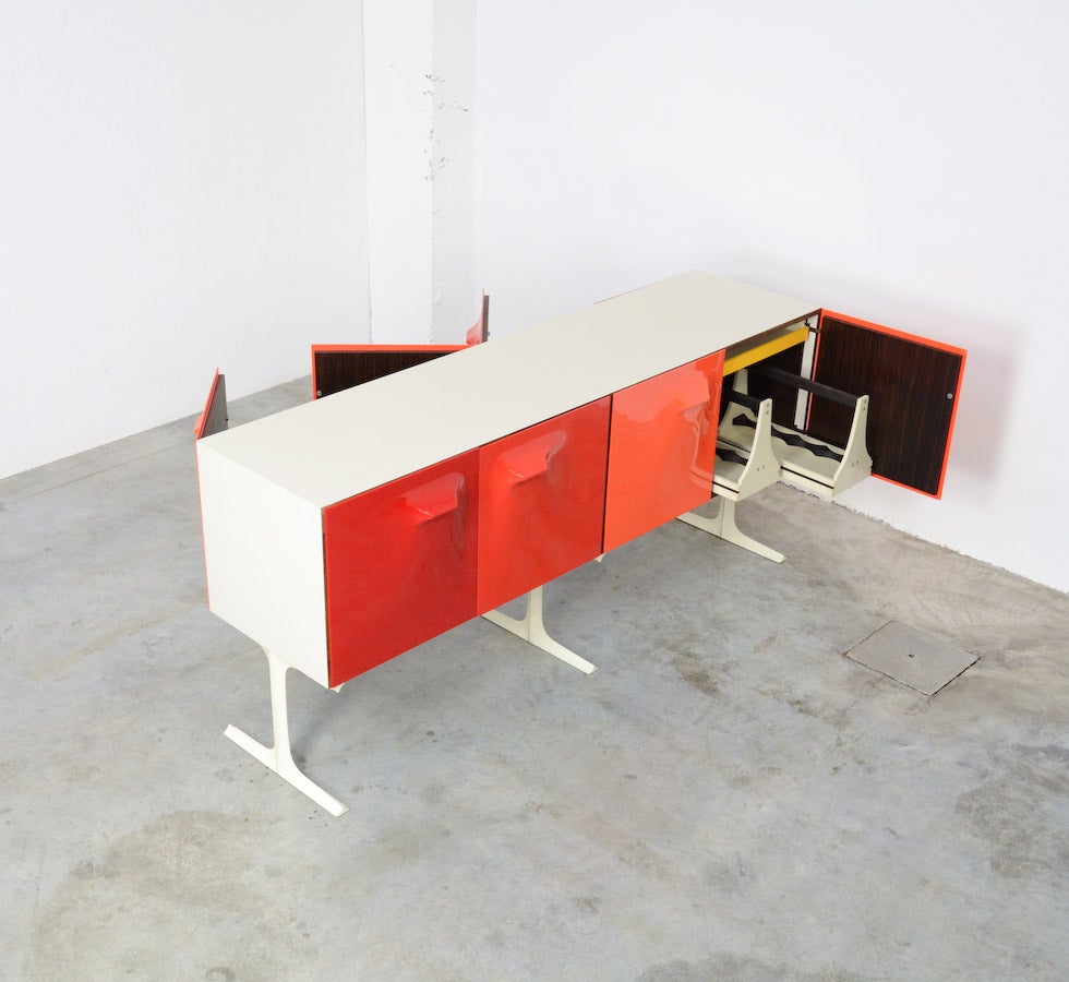 This exclusive and rare Raymond Loewy DF2000 double sided sideboard was manufactured in France in 1965 by “Doubinsky Frères”.
This sideboard has 4 doors on each side, with frontsides in ABS plastic in different shades of orange and red.
The high