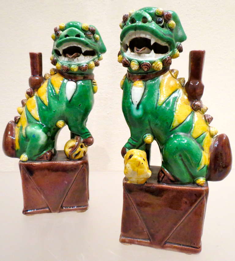 A pair of porcelain foo lions or foo dogs decorated in a pleasing combination of green and yellow enamels. The lions are portrayed seated firmly on their haunches upon a pierced rectangular plinth. Their mouths are open in an almost comic smile,