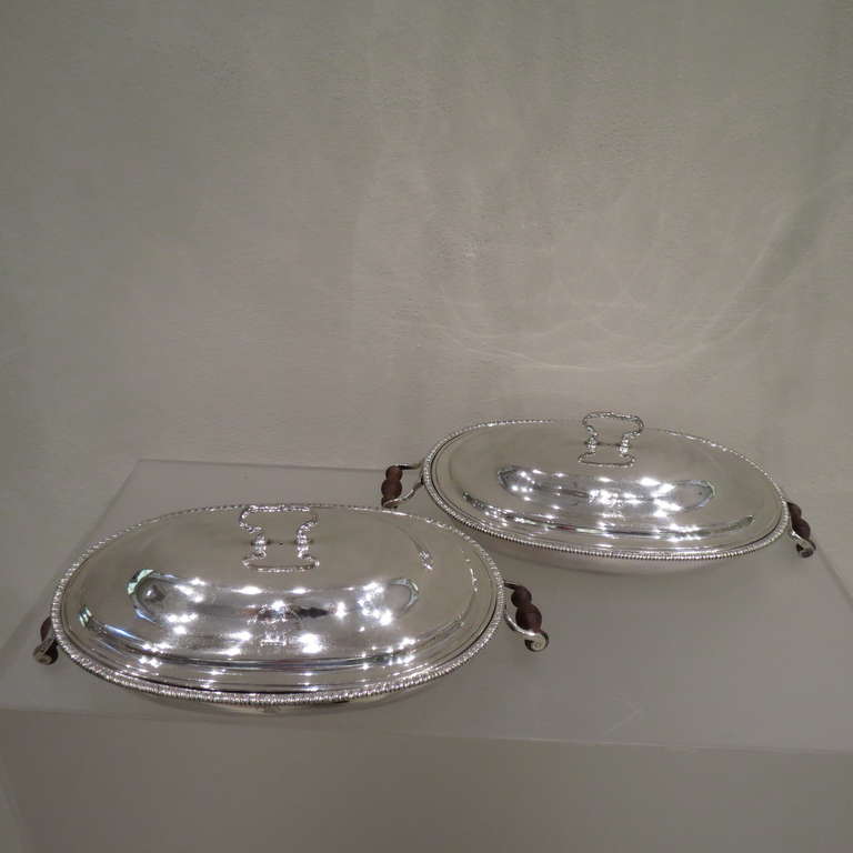 Hallmarked in London in 1773 by John Deacon, this pair of antique, George III, sterling silver entree dishes are oval shaped with a beaded border and hinged handles. The entree dish are (37.6cm) long, (20.6cm) deep, (10.7cm) high and weigh 1140 gr.