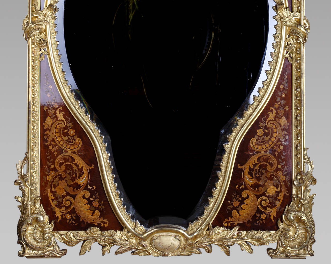 An important gilded wood and stucco mirror. Heart shaped bevelled mirror plate. Rich marquetry ornamentation with mother-of-pearl inlaid. Acanthus leaves, shells and flower baskets motifs surmounted by two putti holding flower garlands. 

Mirrors
