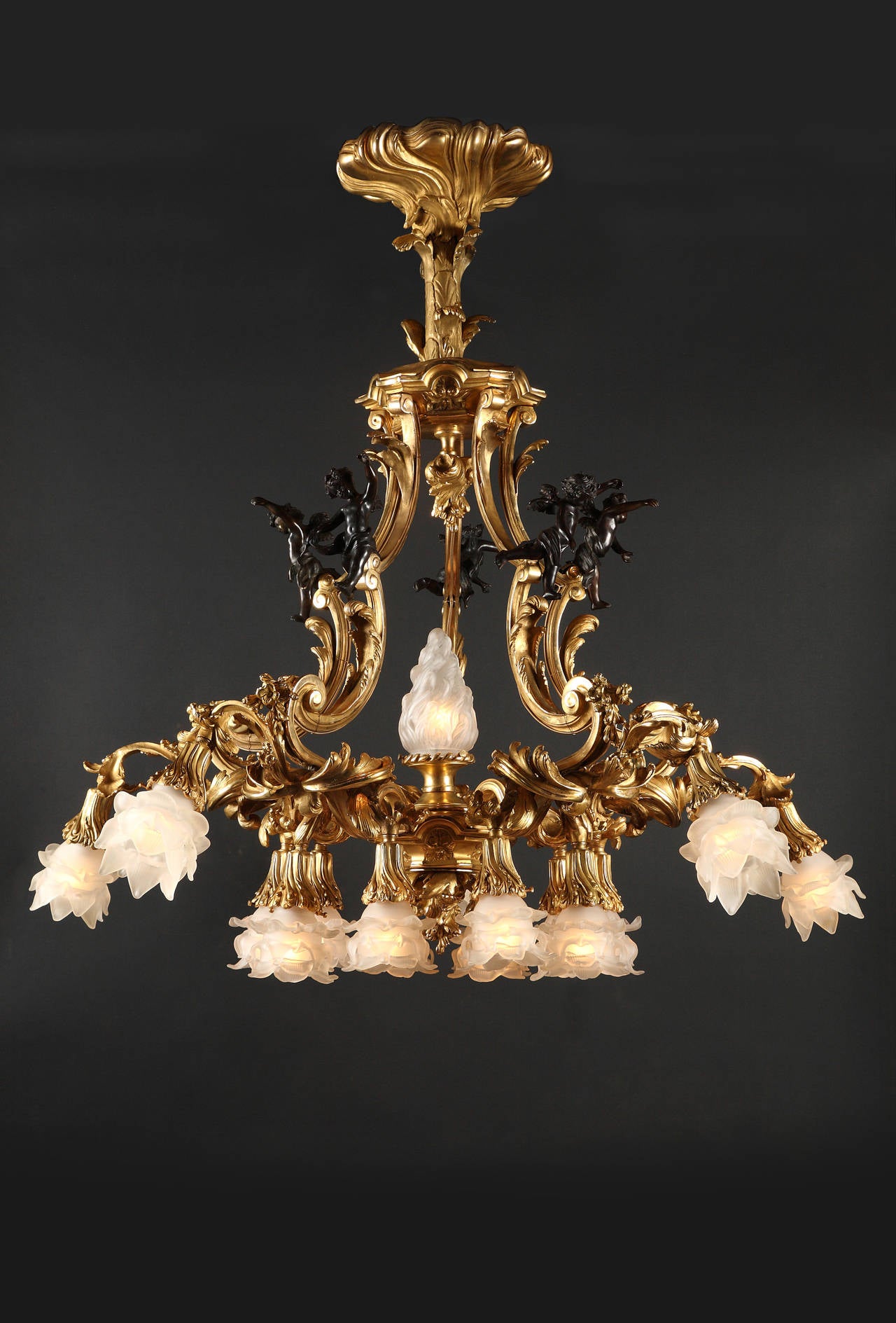 A sumptuous pair of 16 lights gilded bronze chandeliers, ornamented with Louis XV style motifs, such the five patinated putti under an architectural structure, surmounting the foliated scrolled light arms and their flower shaped frosted glass lamp