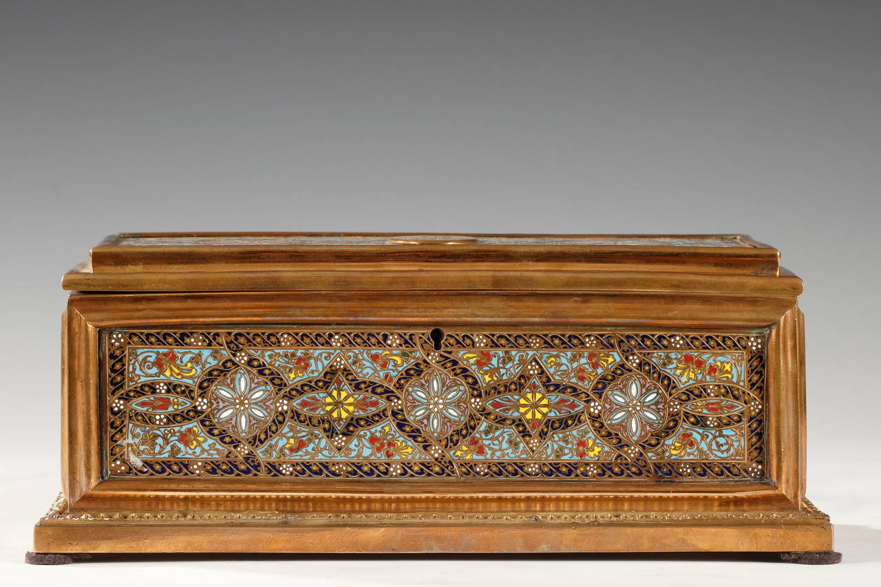 A lovely rectangular box made in gilded bronze, entirely decorated with polychrome “champlevé” enamel rosettes and stylized flowers, and embellish on the top with a monogram. It has preserved its original purple silk velvet lining