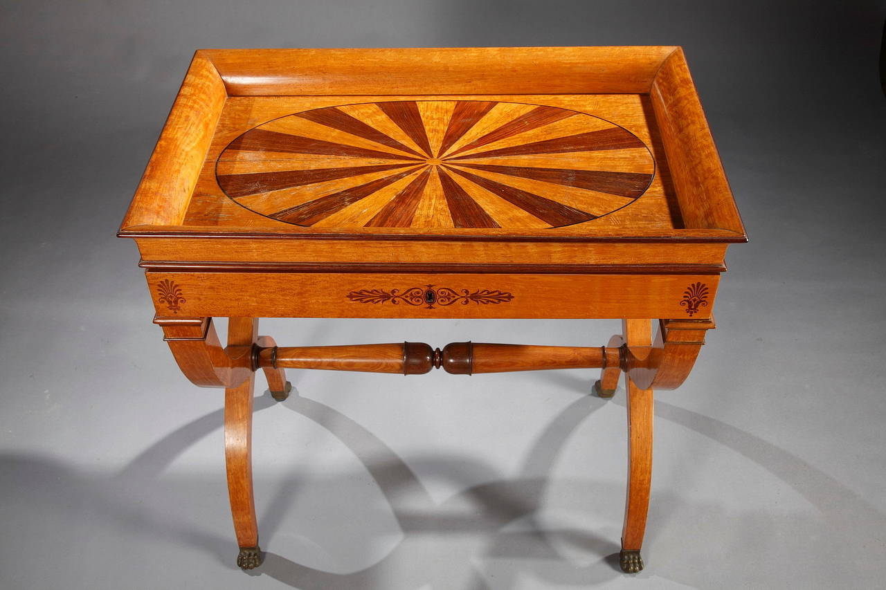 An elegant writing table from the Charles X period, veneered with lemon tree and amaranth. The concave top is adorned with an ellipsoidal two-tone pattern. The belt, decorated with thin stylized ornaments, unveils a sliding writing surface covered