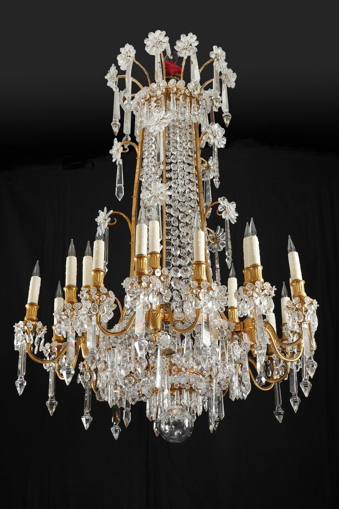 This magnificent chandelier is made of gilded bronze and crystal and presents twenty lights. The tubular shaft composed by garlands made of crystal octogones is adorned with crystal flower crowns. The lower part is fitted with a multitude of crystal