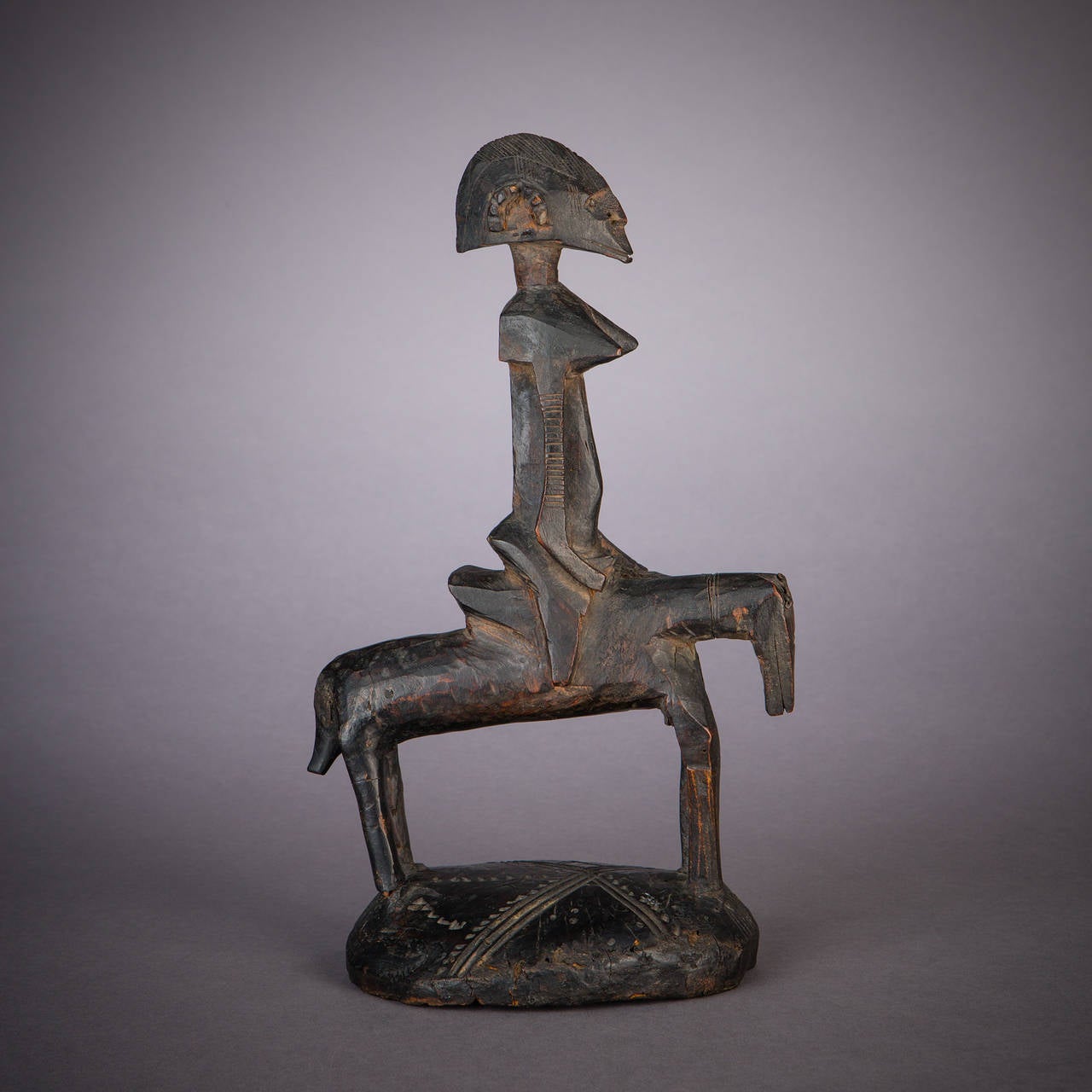 A female rider sits astride a nearly abstracted horse in this strong Senufo equestrian vessel lid. The almost brutal use of angularity in this piece lends it a sense of force or vehemence, expressed in the rigid triangles of chin and chest. On the