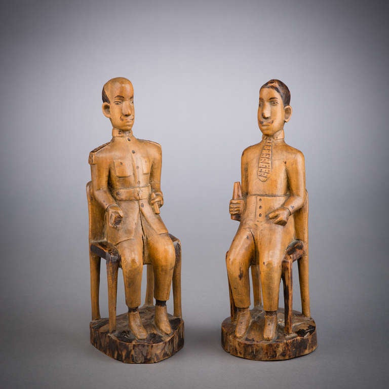 This pair of seated male figures, carved of light-hued wood and treated with pokerwork details, depicts two colonial administrators.  With the advent of colonization,  African carvers began to work European subjects into their repertoires, and in