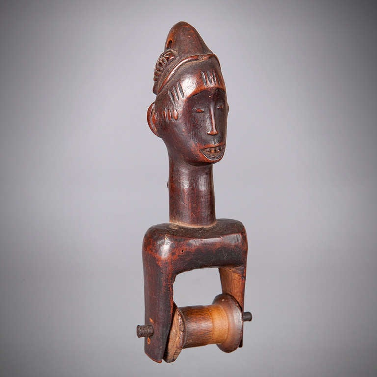 An elegant heddle pulley from the Guro tribe of Ivory Coast.
The pulley has fine scarification patterns on the face and an elegantly carved hairstyle.

Heddle pulleys are used in strip-weaving, a process that uses very small looms to produce