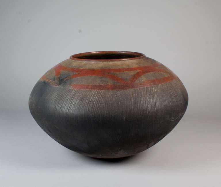 This finely crafted ceramic cooking vessel comes from the Nyakusa peoples of Tanzania or Zambia. A flattened sphere, this pot has shallow vertical ridges leading up to the decorative slip decoration near the top. The black carbon buildup on the base