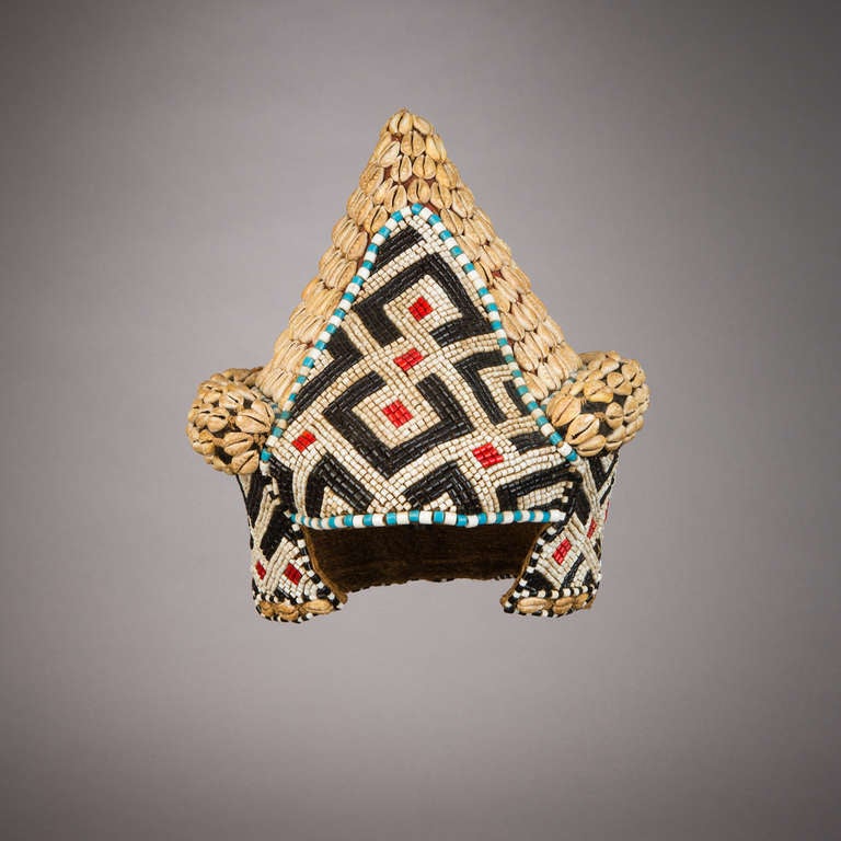 This very rare and elaborately beaded conical hat is called mpaan. The black and white triangular beaded pattern on the sides is called lakwoon, meaning “crochet.” This hat is one of several types of hats worn in council meetings and ceremonies that