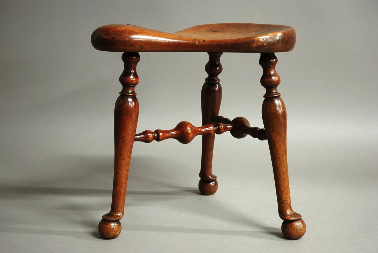 A fine quality late 19th century walnut saddle seat stool.

This unusual stool has a shaped saddle seat of fine patina with three turned stretchers and terminating with pad and ball feet.

Although this stool has the appearance of a model from