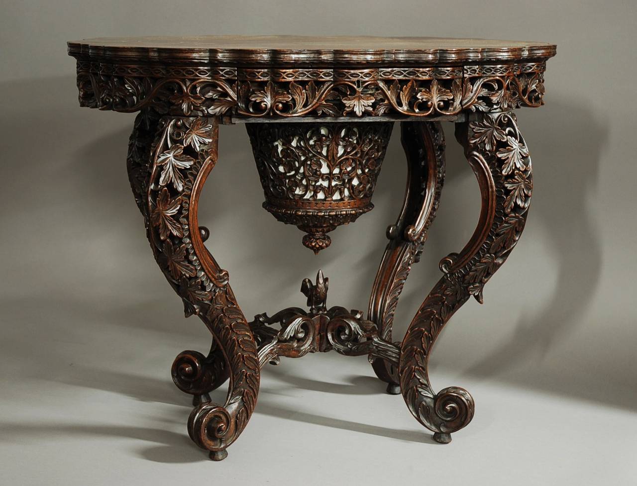 A superb quality Anglo-Indian padouk profusely carved work table.

This table consists of a shaped oval top of superb faded patina (color).

Underneath the top is a shaped and finely carved frieze with a pieced and scrolling leaf design