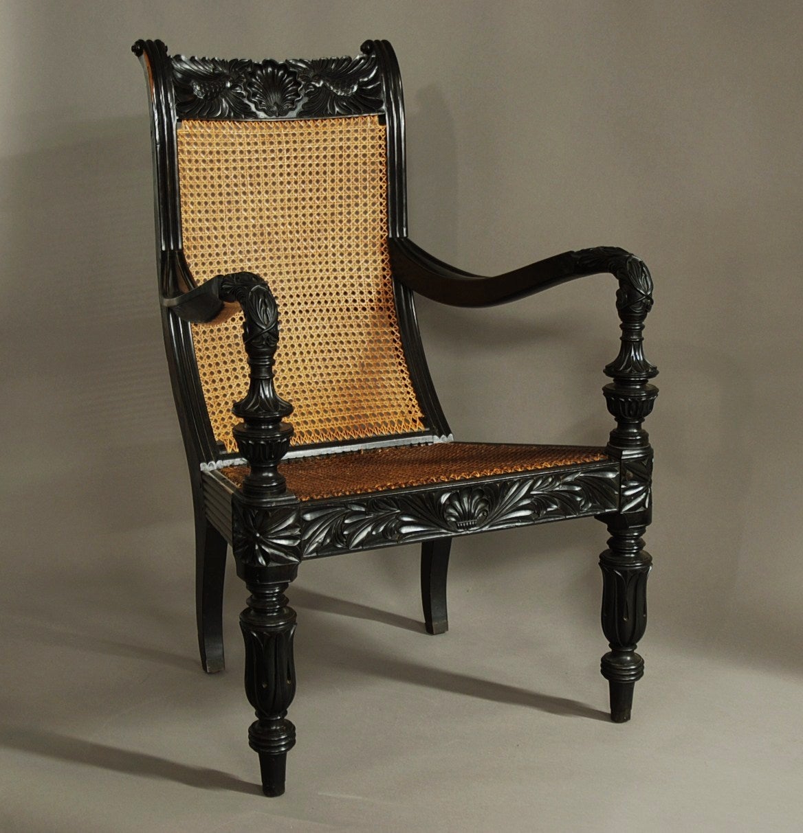 A mid 19th century superb carved solid ebony easy chair from the Galle district (Ceylon/Sri Lanka).

This superb chair consists of a finely carved top rail with central scallop shell carving and finely carved birds to either side.

The uprights