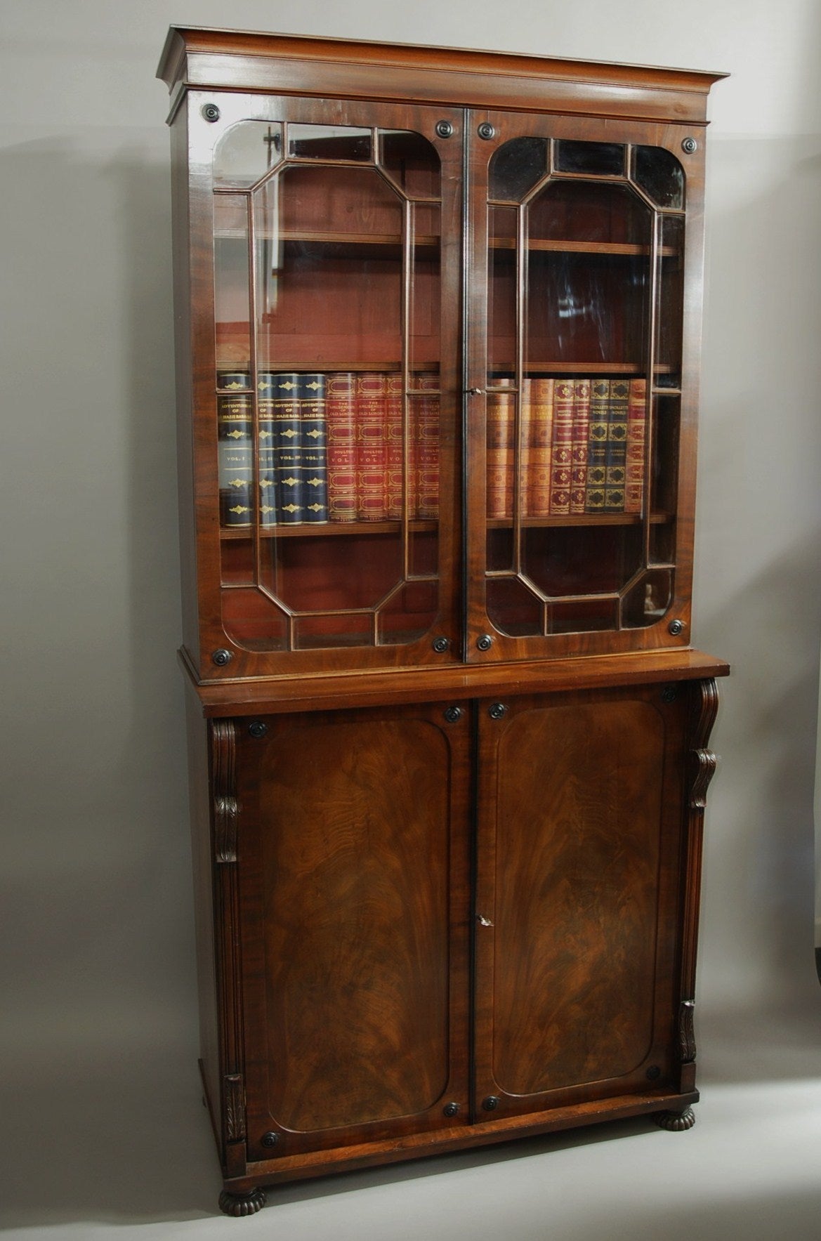 A late 18th-early 19th century mahogany glazed bookcase.

This bookcase consists of a cornice with a shaped moulding with two astragal glazed doors below.

The doors consist of ebonised paterae to each corner with ebonised beading to the
